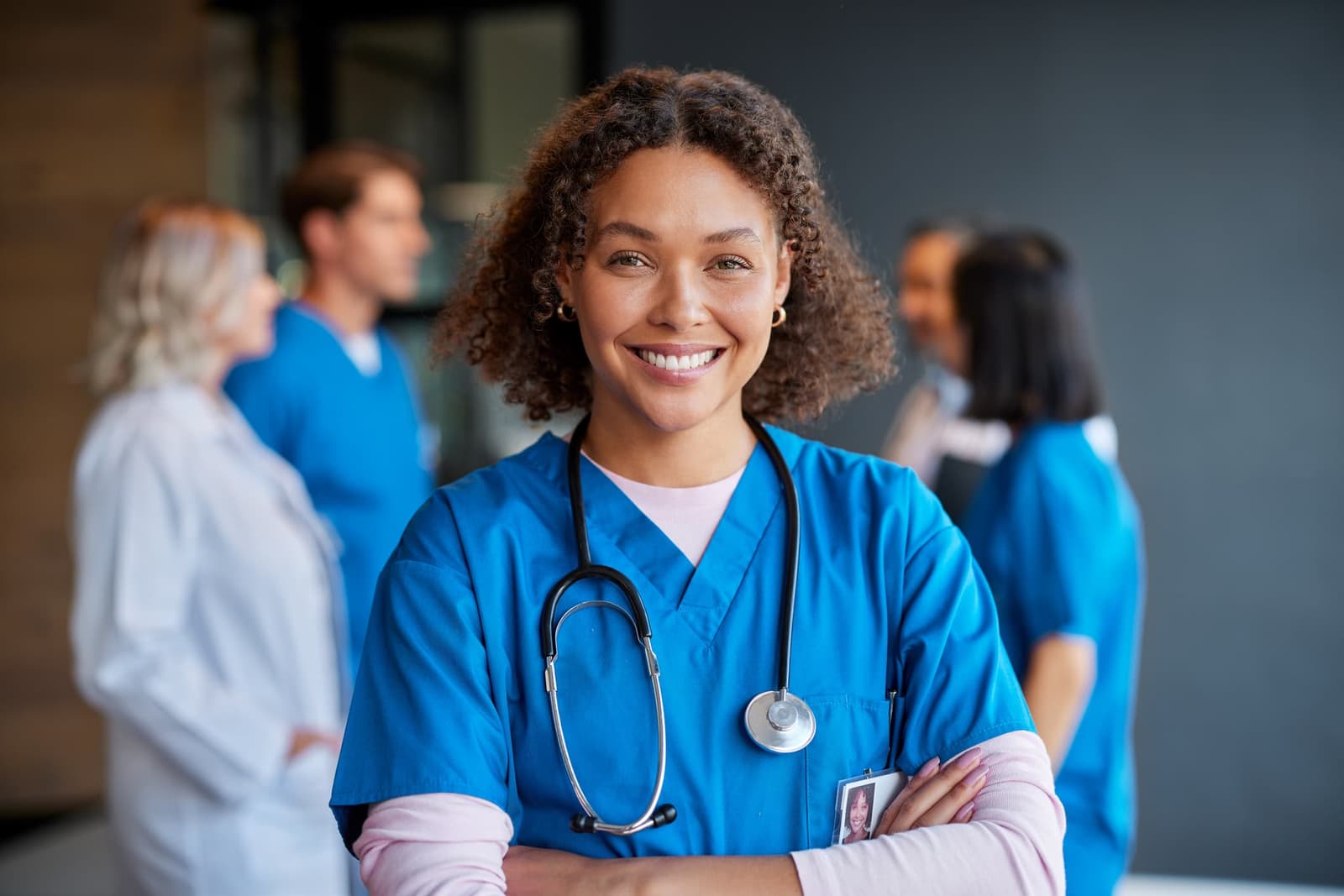 Infirmière diplômée d'État souriante en tenue médicale bleue avec stéthoscope, équipe soignante en arrière-plan