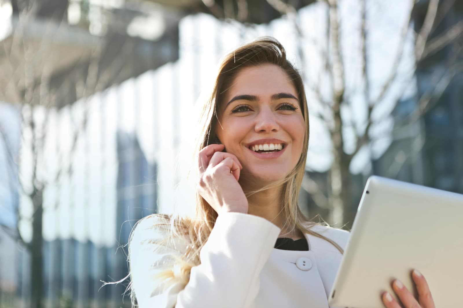Photo d'une jeune femme souriante tenant une tablette devant un immeuble de bureaux