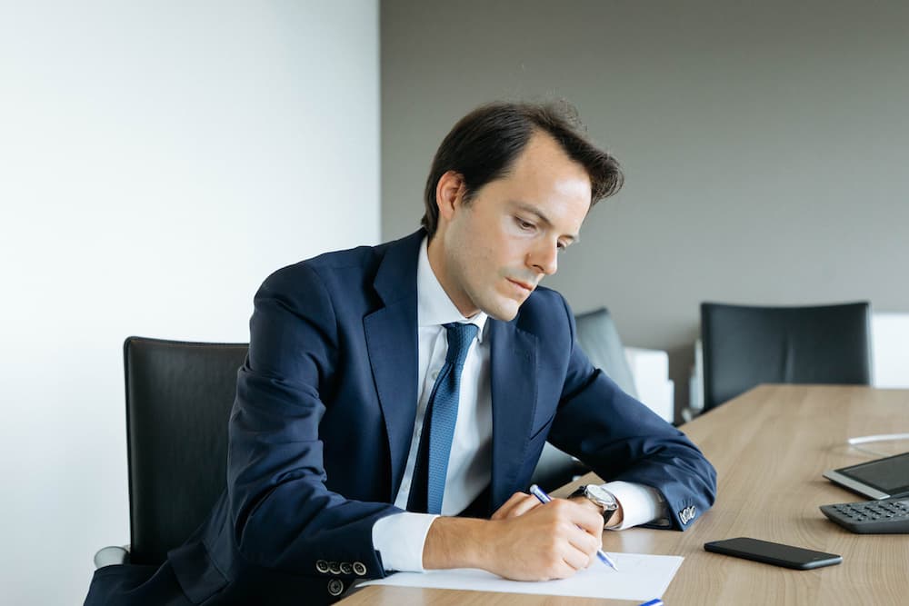Photo d'un homme en costume bleu marine écrivant sur un document dans une salle de réunion