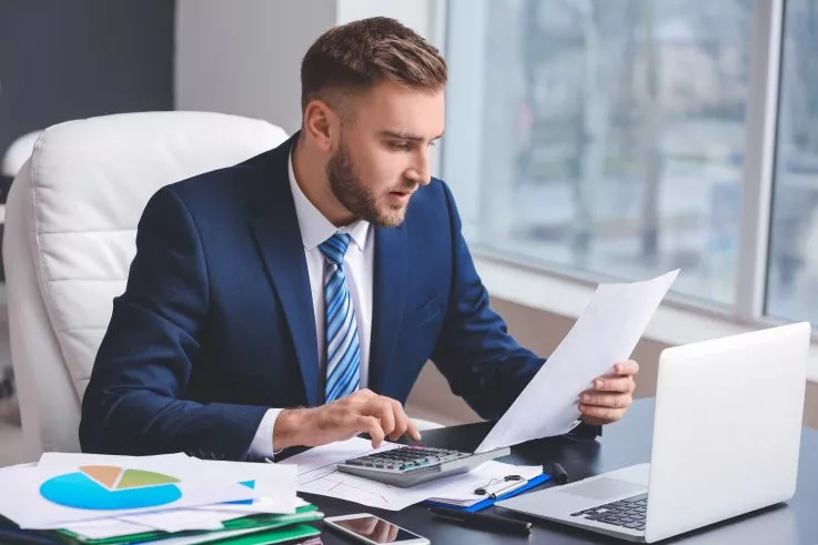 Photo d'un fiscaliste en costume utilisant une calculatrice et examinant un document au bureau