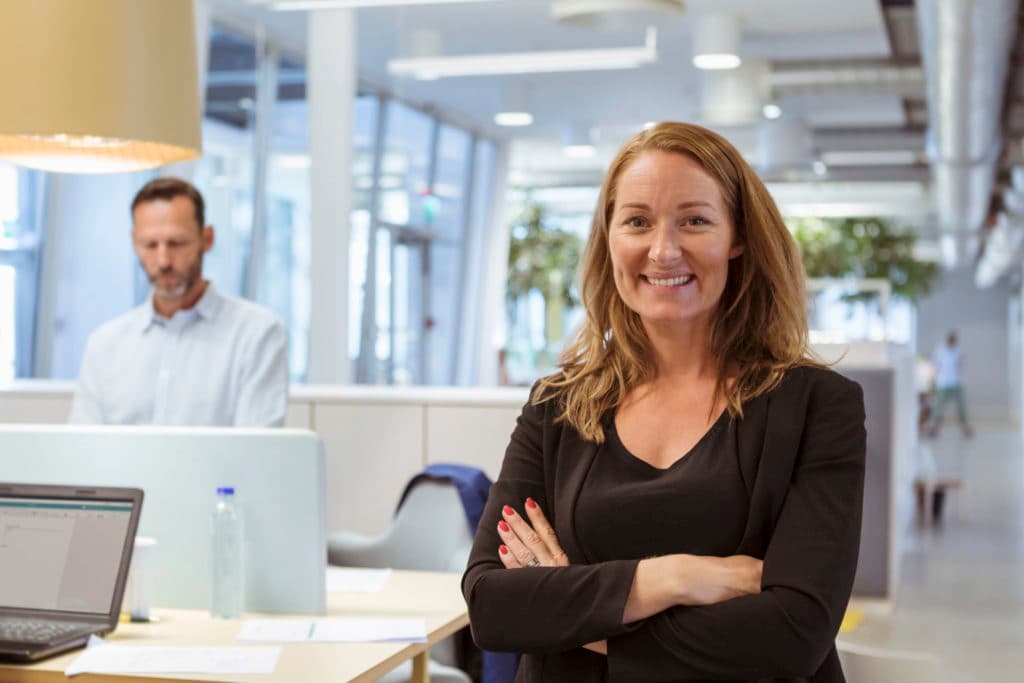 Photo d'une femme souriante bras croisés en haut noir dans un open space moderne