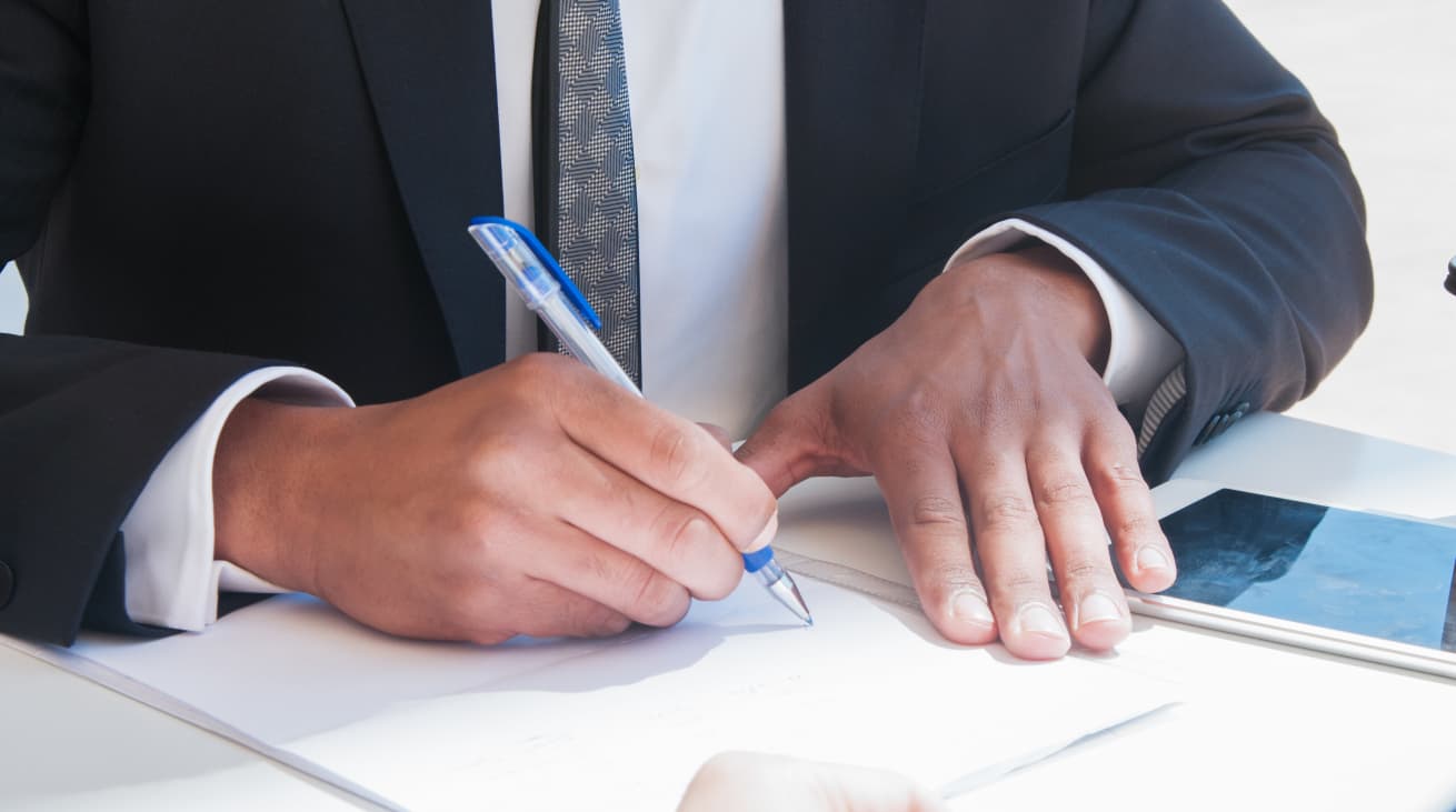 Photo d'un professionnel en costume noir signant un document avec un stylo bleu sur un bureau