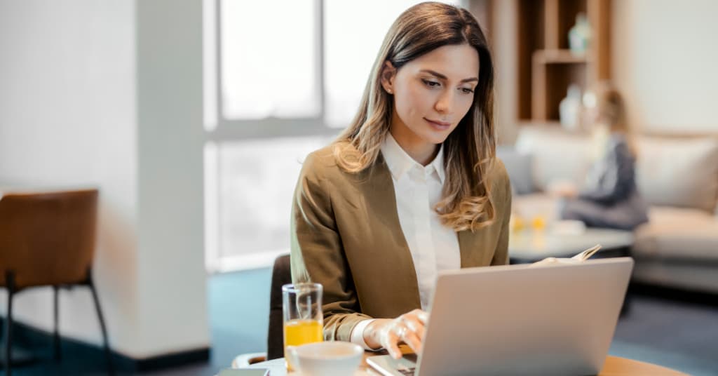 Photo d'une femme en blazer kaki et chemise blanche travaillant sur un ordinateur portable dans un bureau