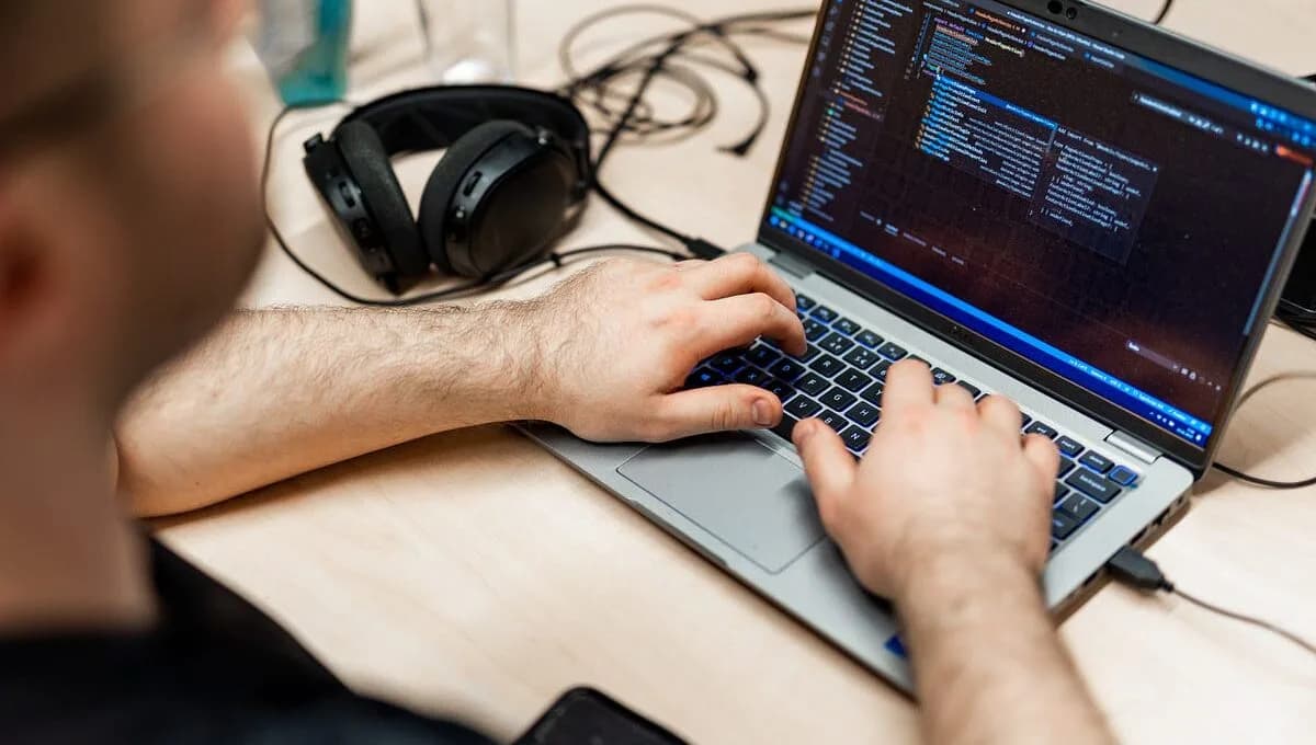 Photo d'un développeur tapant du code sur un ordinateur portable avec un casque audio sur le bureau