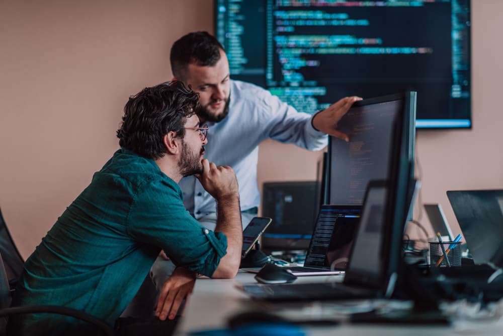 Deux architectes logiciel analysant du code source sur des écrans multiples dans un environnement de développement