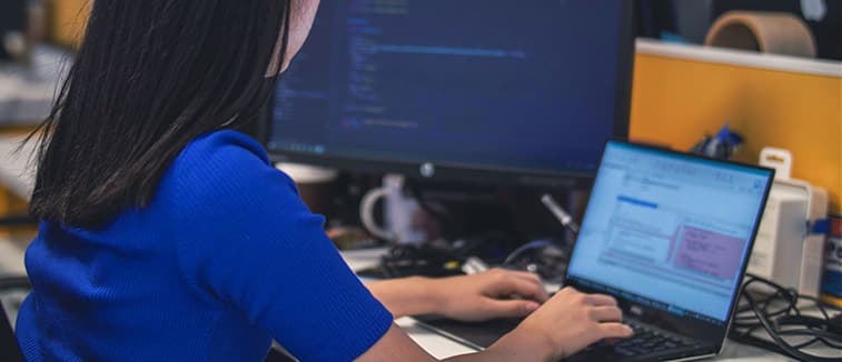 Développeuse front-end codant sur un ordinateur portable avec écran de code en arrière-plan dans un bureau