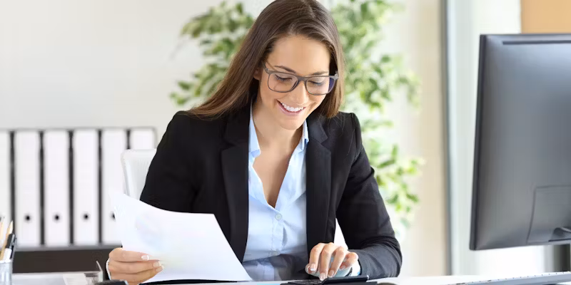Trésorière souriante en tailleur consultant des documents financiers à son bureau avec ordinateur