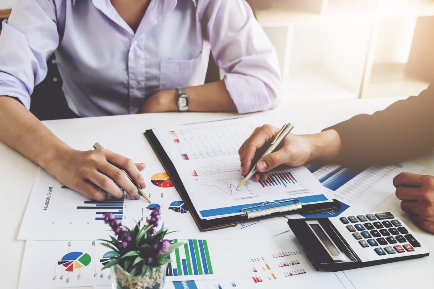 Photo de deux professionnels analysant des graphiques financiers et des rapports sur un bureau