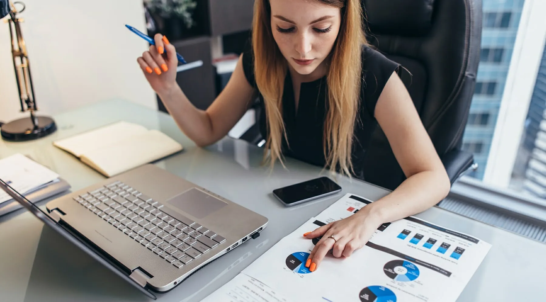 Photo d'une femme analysant des graphiques financiers imprimés devant son ordinateur portable au bureau