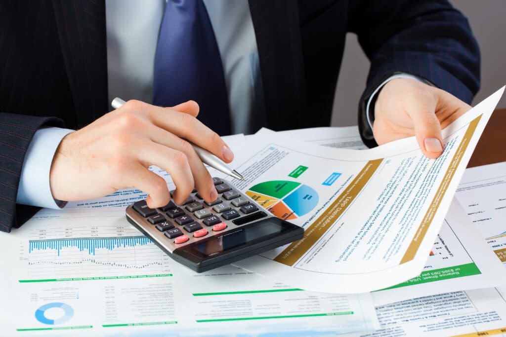 Photo d'un homme en costume utilisant une calculatrice entouré de rapports financiers avec graphiques
