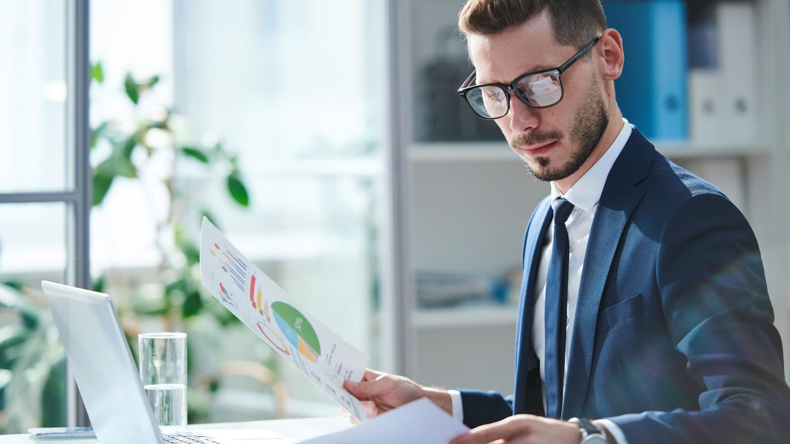 Photo d'un homme en costume avec lunettes consultant un rapport financier avec graphiques au bureau