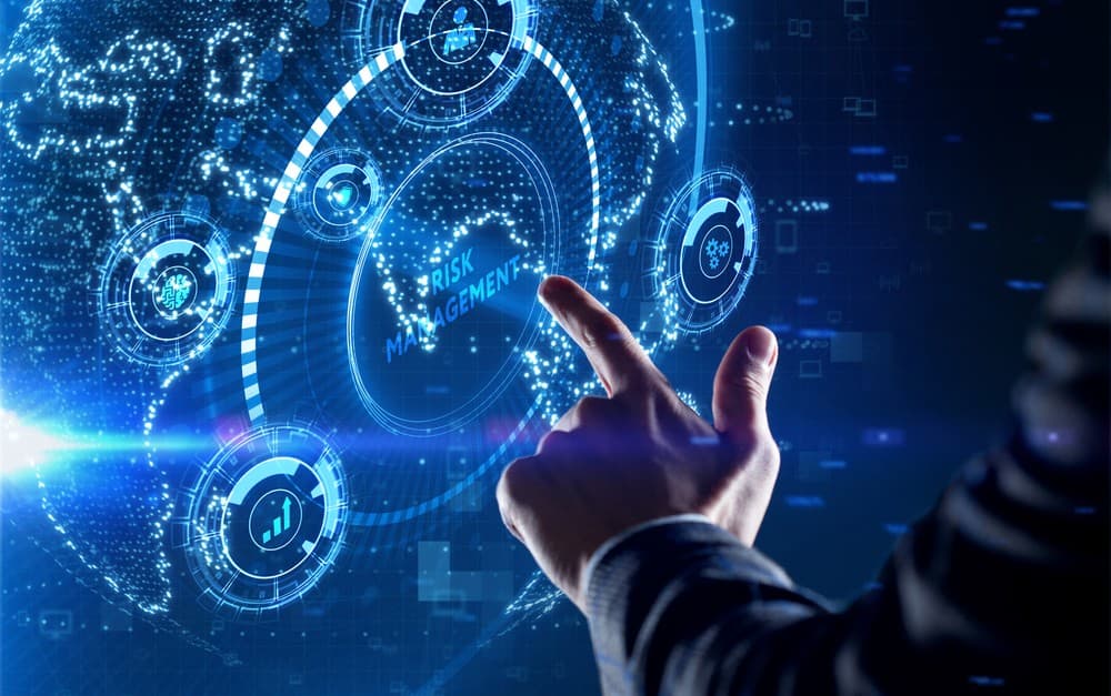 Photo d'une main pointant vers un écran holographique affichant Risk Management et indicateurs