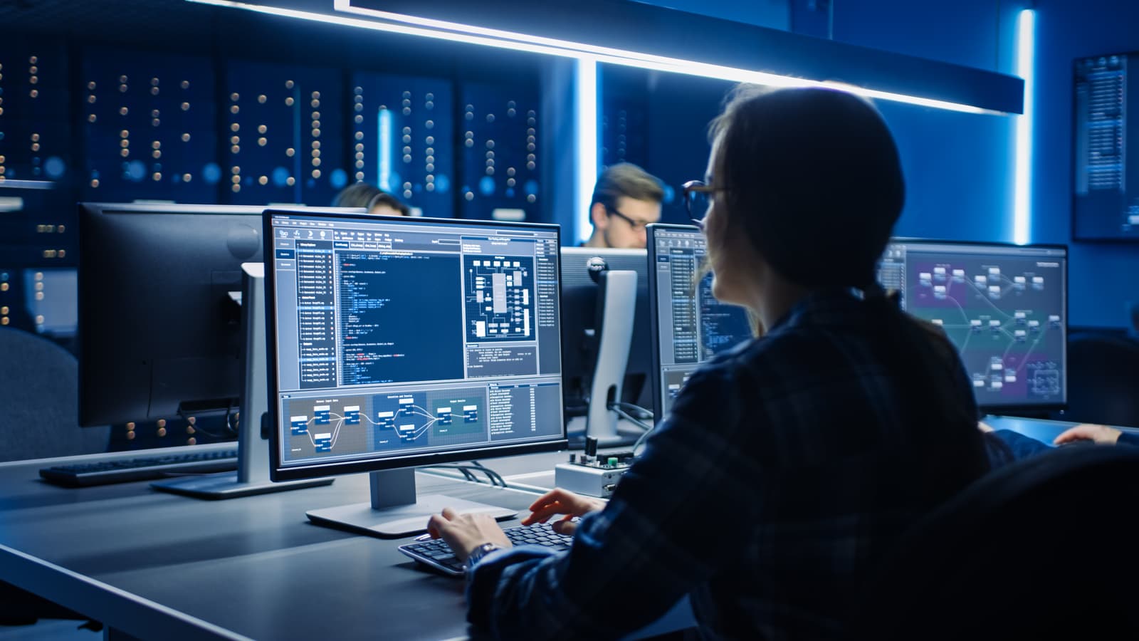 Photo d'une ingénieure travaillant sur des écrans affichant du code et des flux de données dans un data center