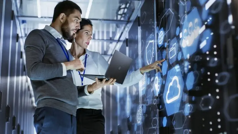 Photo de deux professionnels avec un ordinateur portable consultant des icônes cloud dans un data center