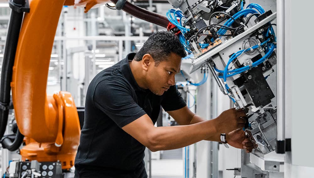 Photo d'un ingénieur en polo noir ajustant un bras robotique orange dans une usine