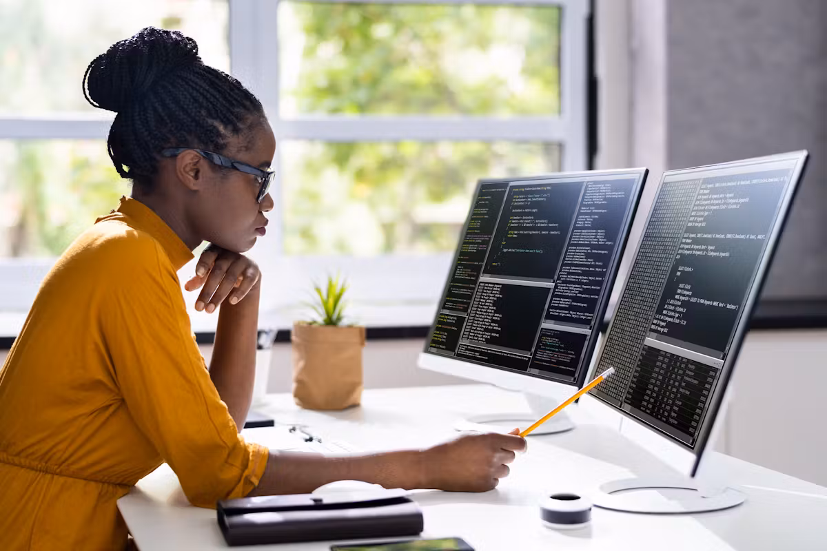 Ingénieure logiciel concentrée lisant du code source sur trois écrans dans un bureau lumineux