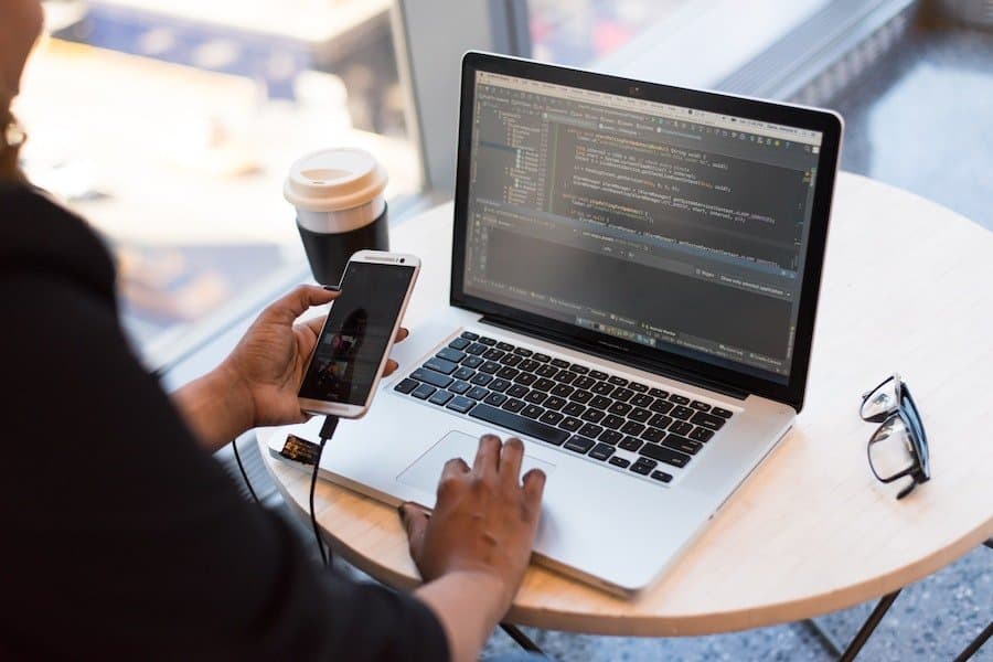 Photo de développeur testant une application sur smartphone connecté à un ordinateur portable