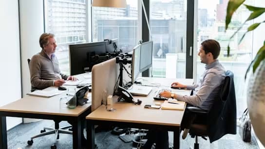 Photo de deux collègues travaillant face à face à leurs bureaux avec ordinateurs