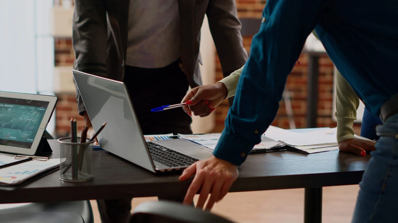 Photo de professionnels debout autour d'un bureau avec ordinateur portable, tablette et rapports financiers