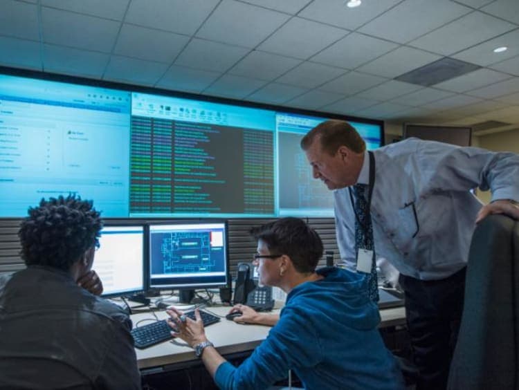 Photo d'une équipe dans un centre de supervision informatique avec grands écrans affichant des données