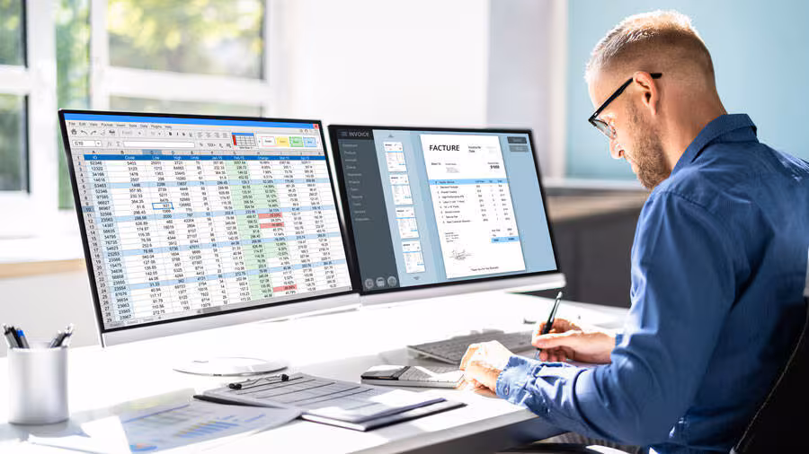 Comptable travaillant sur des tableurs financiers et factures sur un poste à double écran dans un bureau