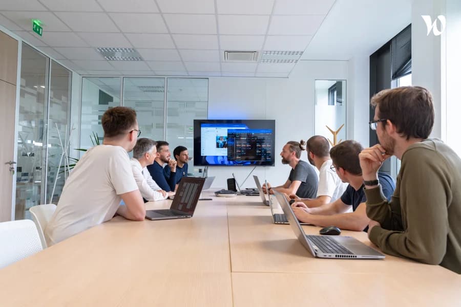 Photo d'une équipe en réunion dans une salle de conférence avec laptops et grand écran