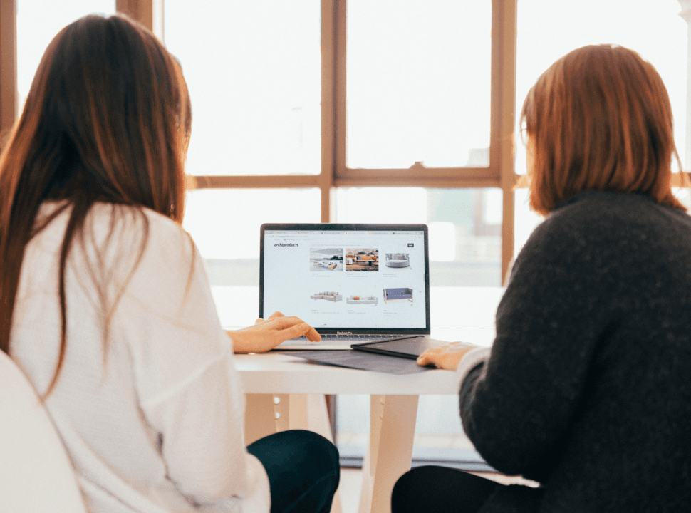Photo de deux femmes vues de dos consultant un site web sur un ordinateur portable