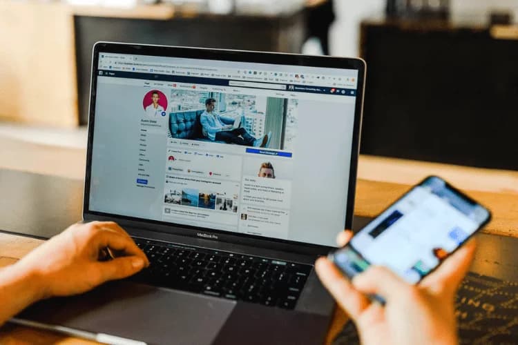 Photo d'une personne consultant un profil sur les réseaux sociaux sur un laptop avec un smartphone