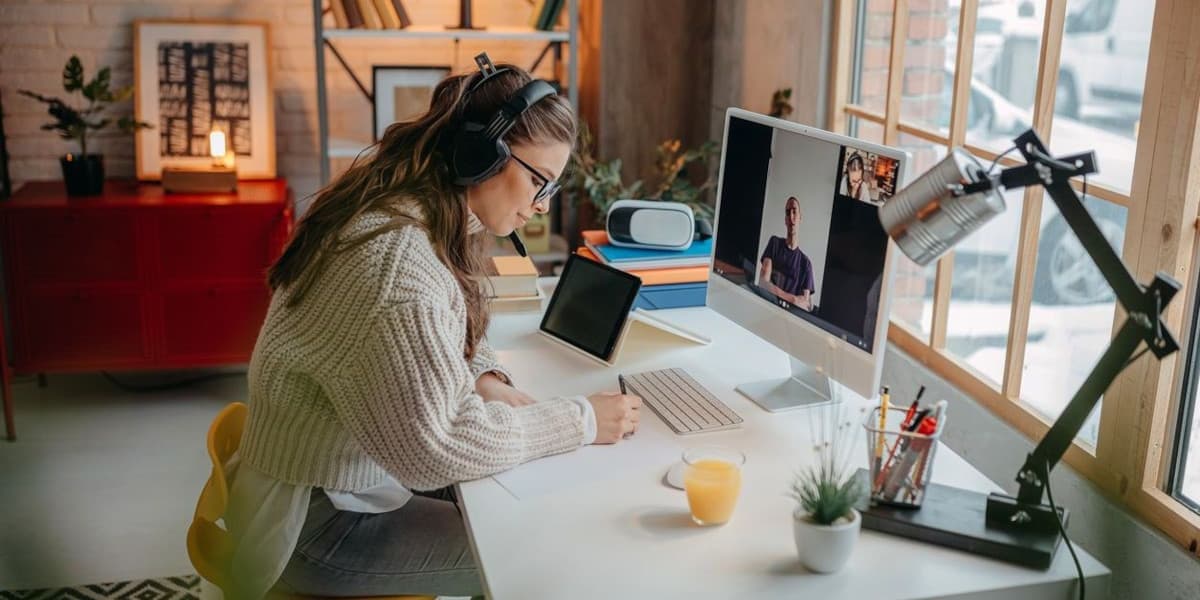 Photo d'une femme avec un casque audio en visioconférence devant son bureau avec micro et tablette