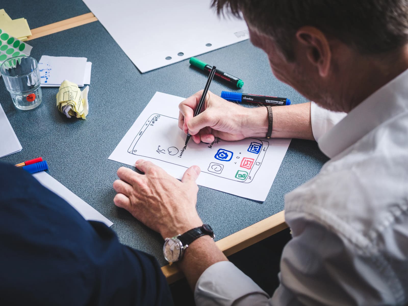 Photo d'un homme dessinant un wireframe d'interface mobile avec des feutres de couleur