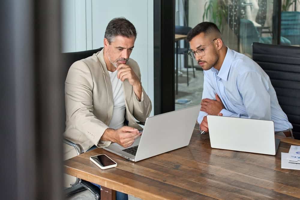 Photo de deux hommes en tenue professionnelle discutant devant des ordinateurs portables au bureau