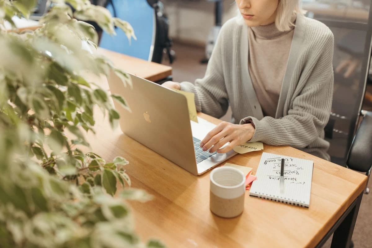 Photo d'une femme travaillant sur un MacBook avec des post-it et un carnet sur un bureau en bois