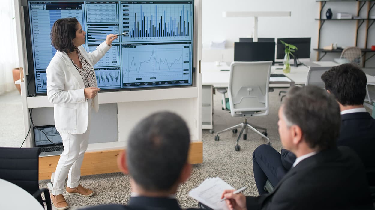 Finance manager présentant des graphiques financiers et indicateurs boursiers devant des collègues en réunion