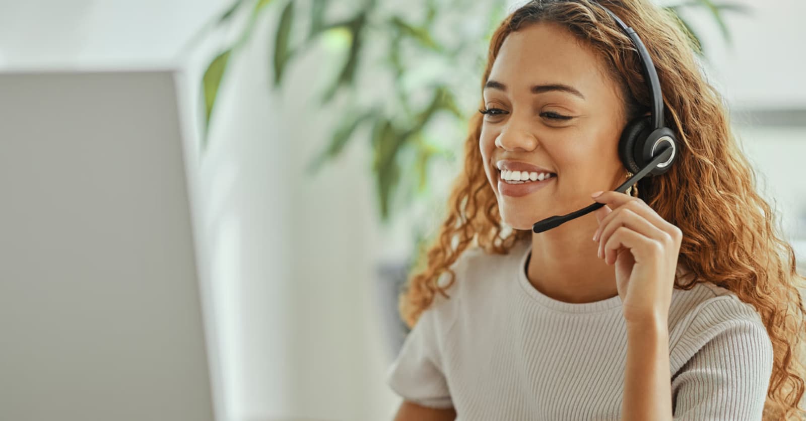 Photo d'une femme souriante avec un casque-micro parlant devant son écran d'ordinateur