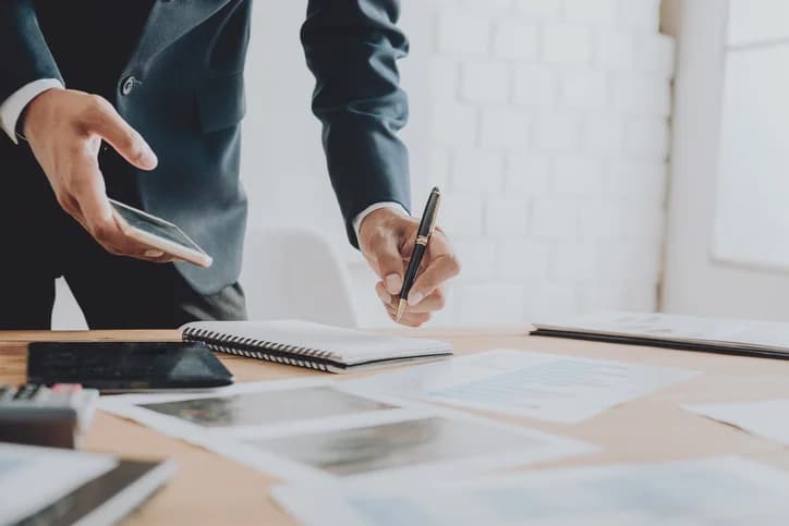 Photo d'un professionnel en costume prenant des notes sur un bureau avec smartphone et documents