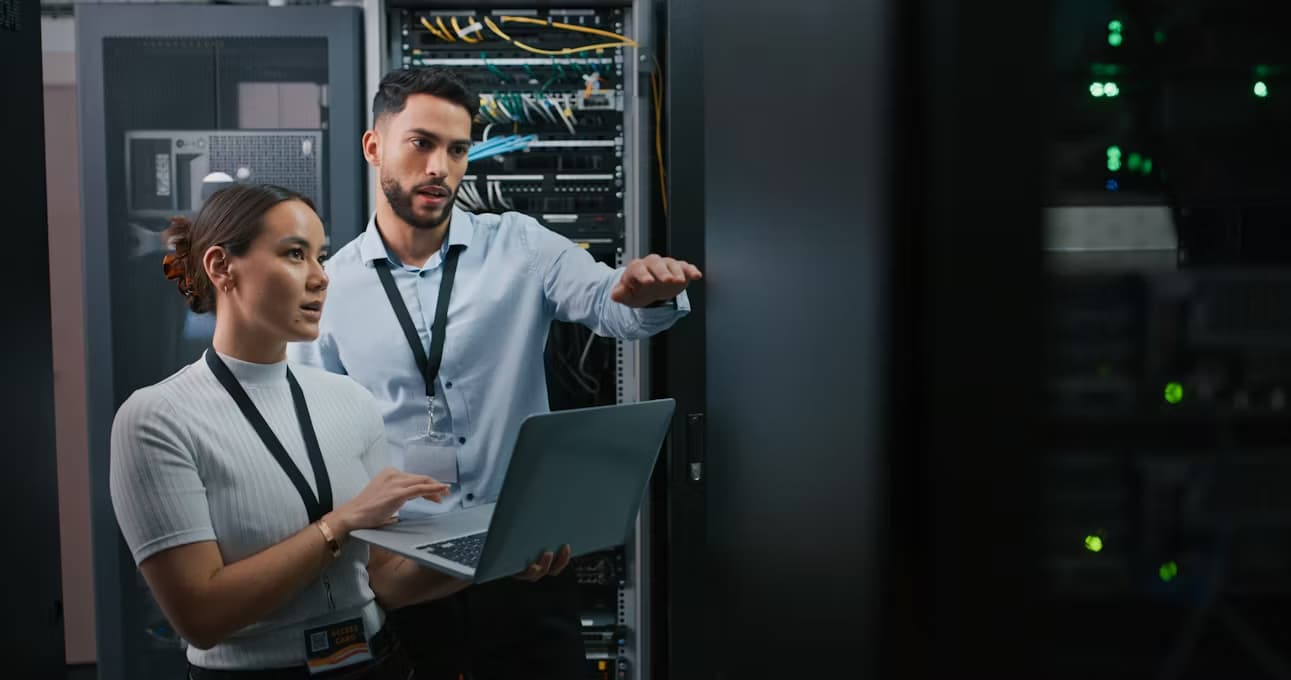 Photo de deux ingénieurs avec un portable devant des baies de serveurs informatiques