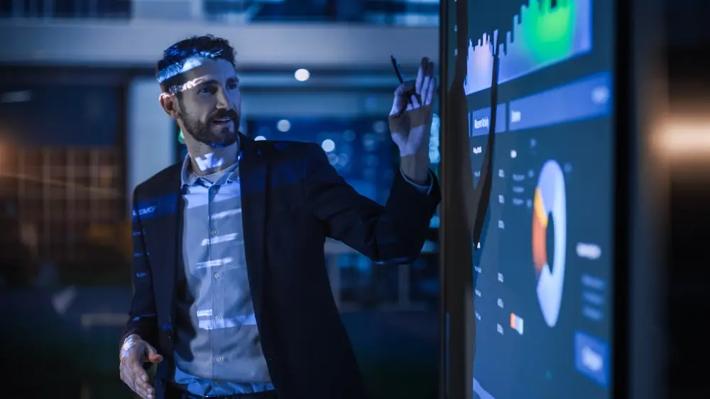 Photo d'un homme en costume présentant des graphiques sur un grand écran interactif
