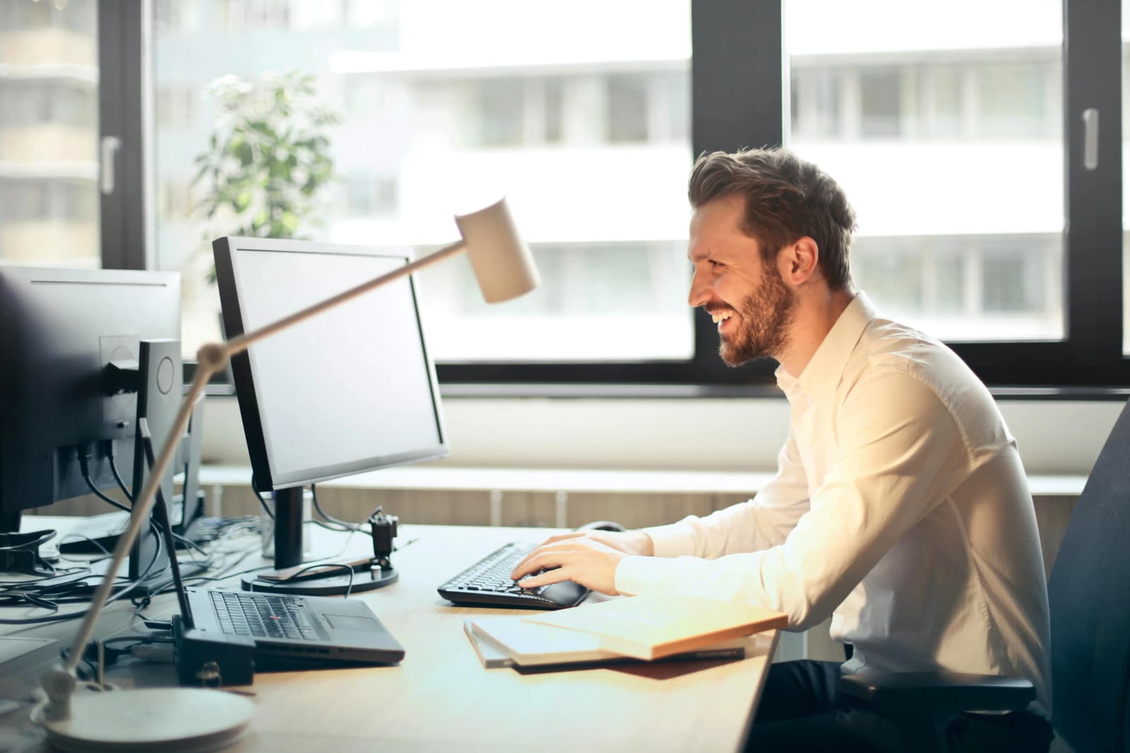 Photo d'un homme souriant en chemise blanche travaillant sur ordinateur dans un bureau lumineux