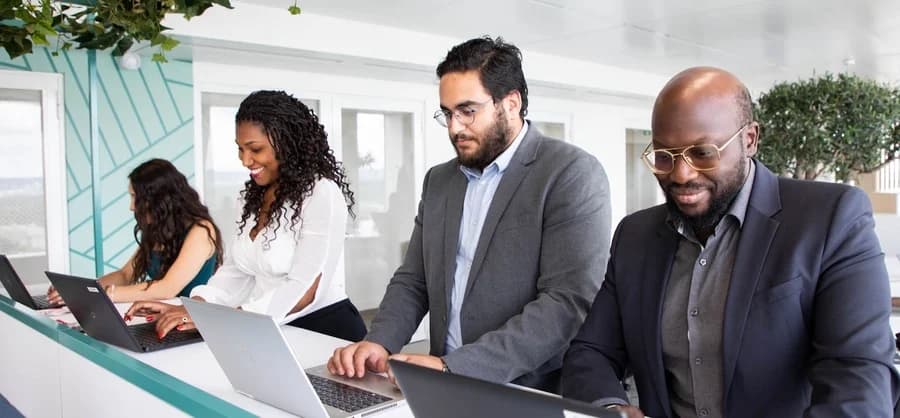 Photo de quatre professionnels travaillant côte à côte sur leurs ordinateurs portables dans un bureau