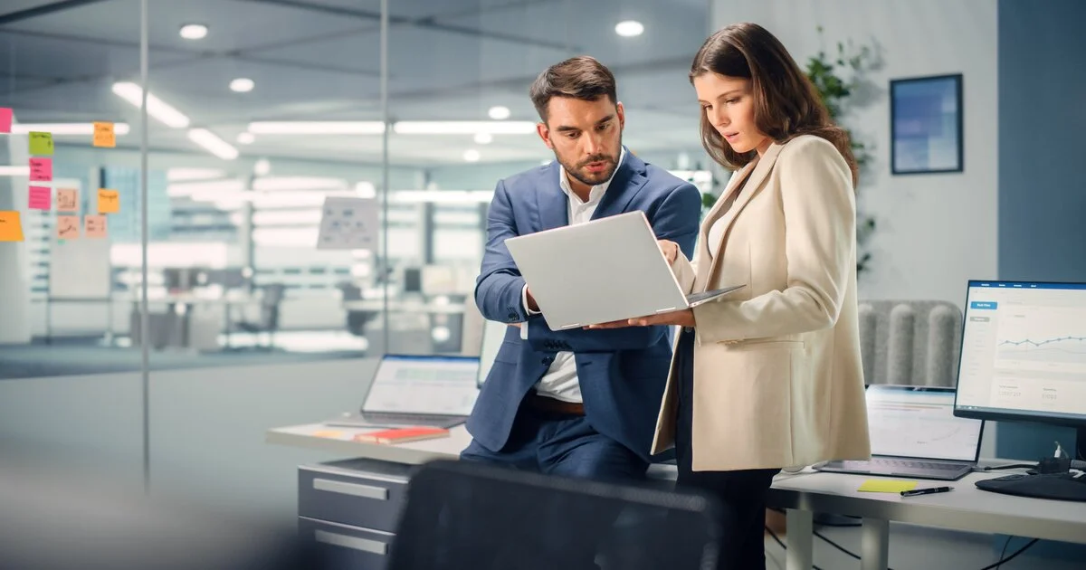 Photo de deux commerciaux en tenue professionnelle analysant des données sur un ordinateur portable au bureau