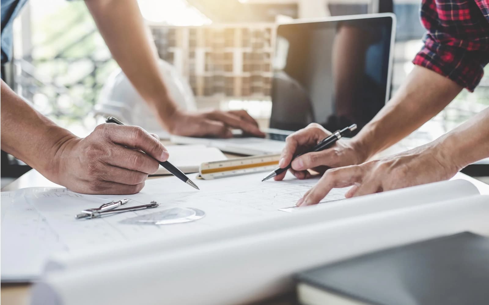 Photo de mains travaillant sur des plans techniques avec compas, règle et ordinateur portable sur un bureau