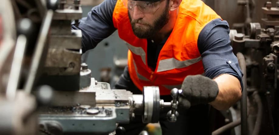 Photo d'un technicien en gilet orange intervenant sur une machine-outil industrielle