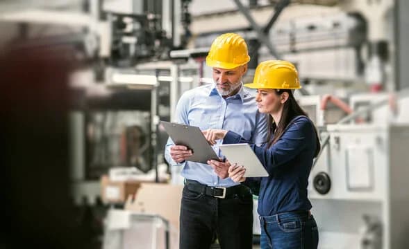 Photo de deux responsables en casques jaunes consultant un dossier dans une usine