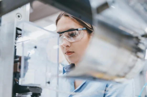 Photo d'une ingénieure avec lunettes de protection observant une machine en atelier