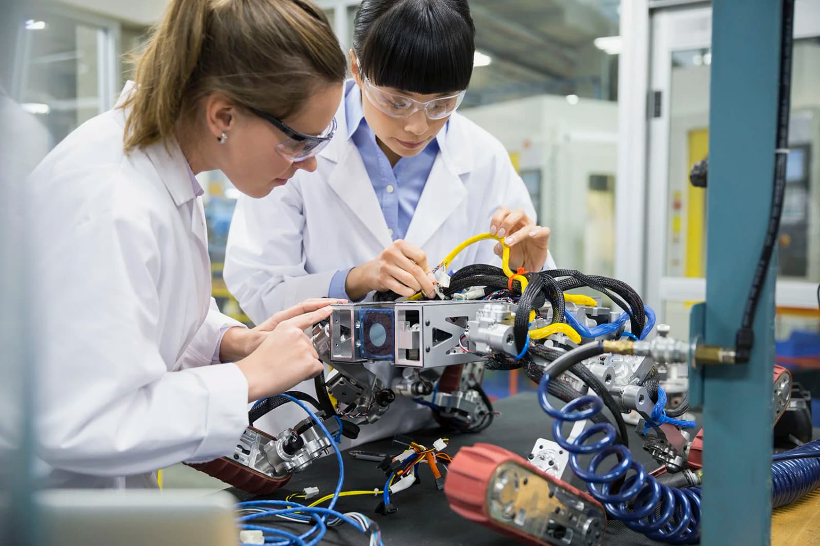 Photo de deux ingénieures en blouses blanches assemblant un système robotique en laboratoire