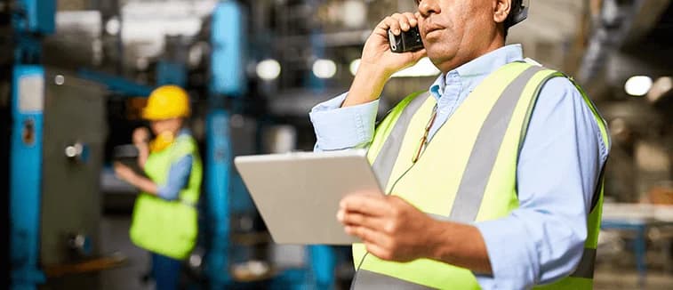 Photo d'un superviseur en gilet jaune au téléphone avec une tablette en usine