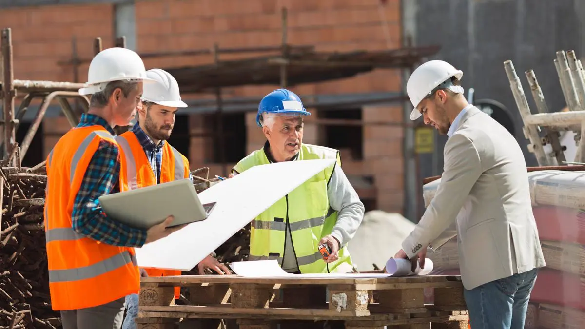 Photo de quatre professionnels en casques discutant avec des plans sur un chantier