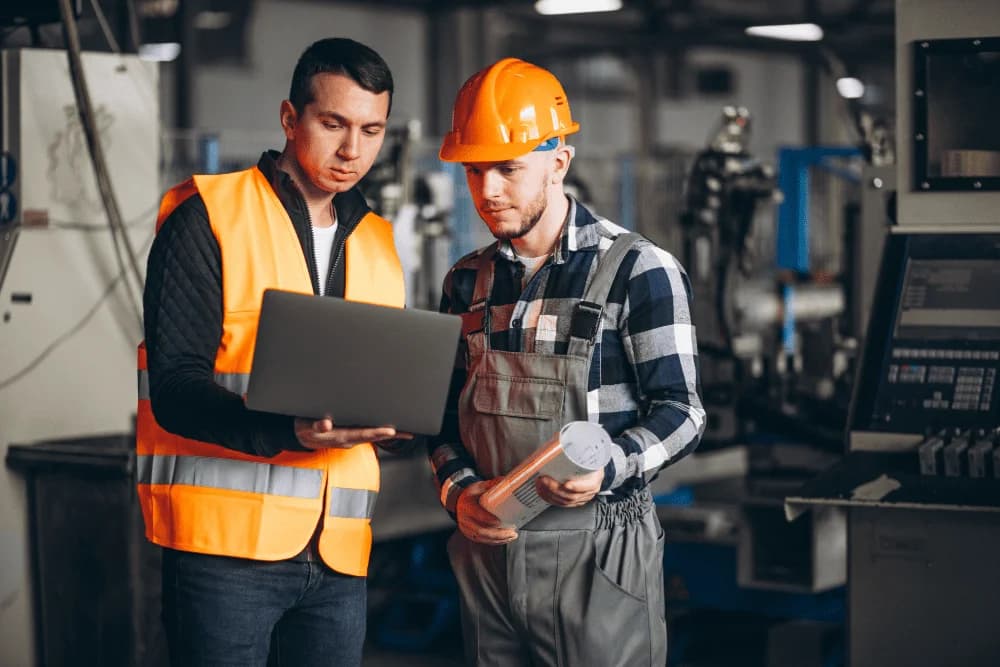 Photo de deux techniciens en gilets orange consultant un ordinateur portable en usine