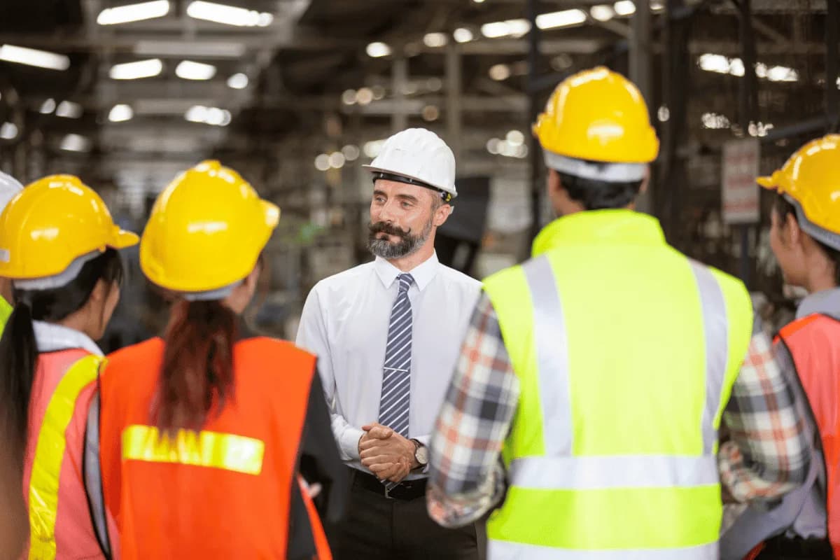 Photo d'un responsable en casque blanc briefant des ouvriers en gilets dans une usine