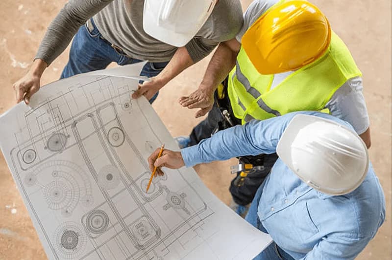 Photo de trois ouvriers en casques examinant des plans techniques sur un chantier
